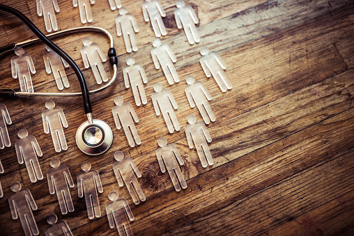 A wooden background with small wooden people shapes and a stethoscope