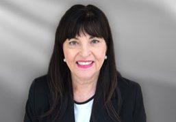Photo of a white lady with dark shoulder length hair including a fringe with white earrings and pink lipstick
