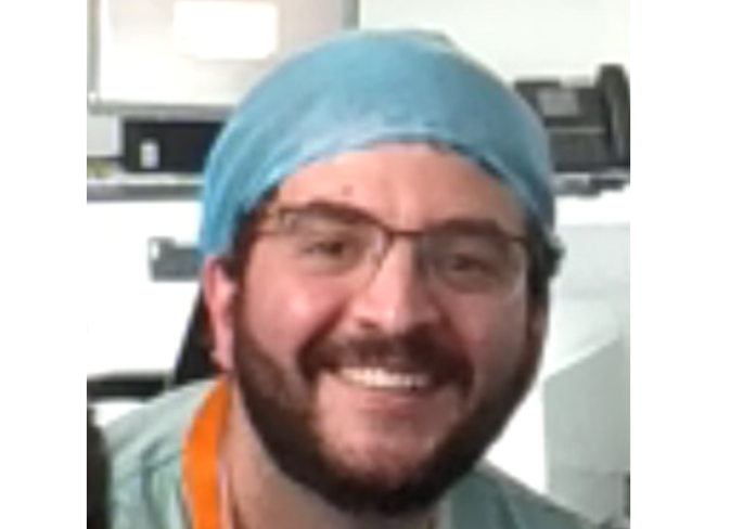 Photo of man wearing glasses and a surgical hair covering who has dark short facial hair